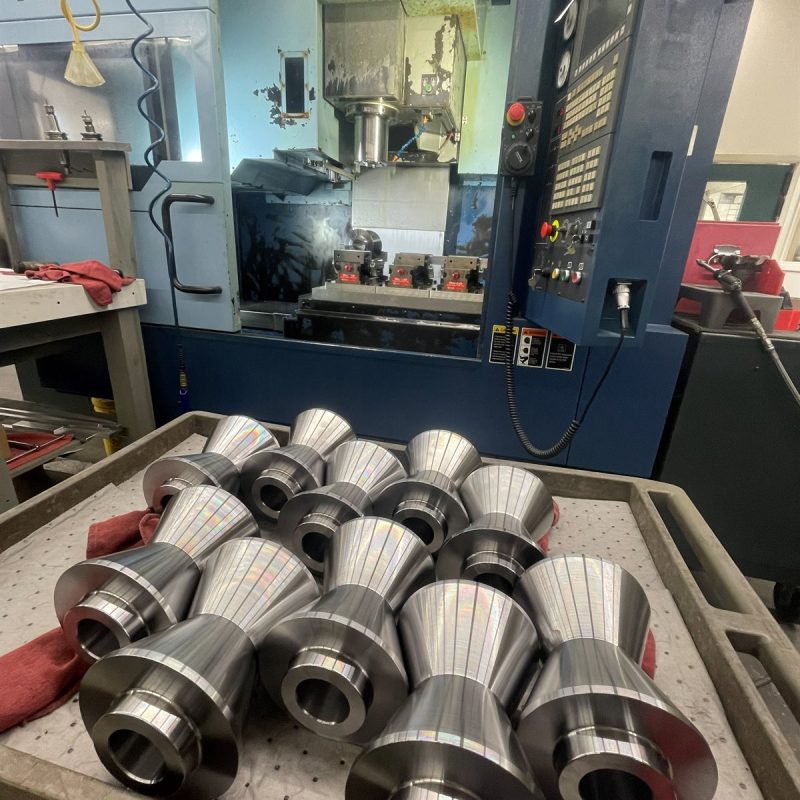 Machined cylindrical parts in front of a Matsuura VX-1000 mill